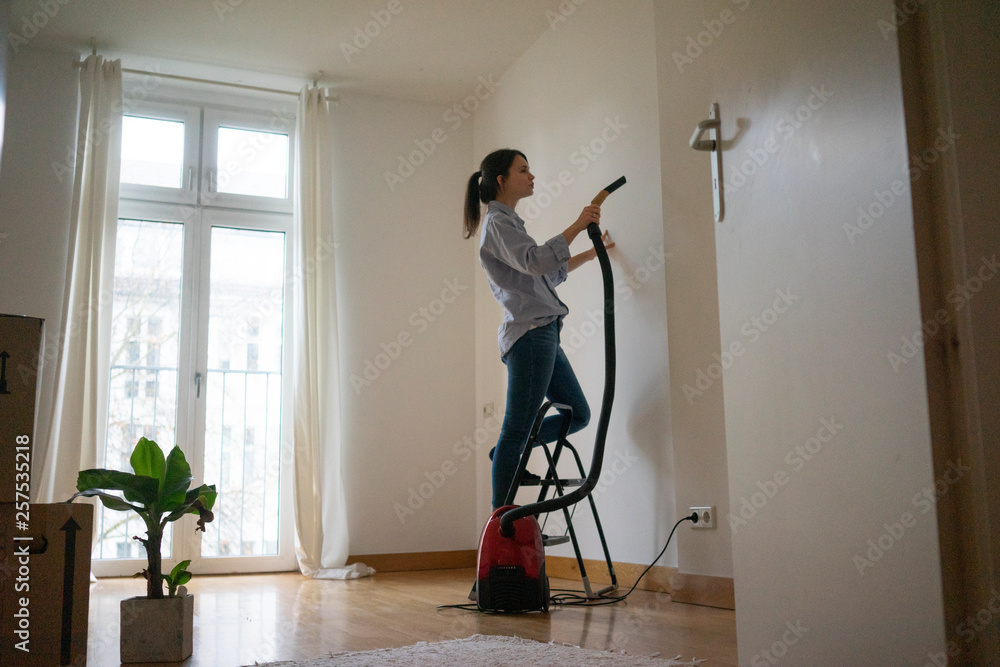 Young woman standing on step ladder, hoovering her new home Young woman standing on step ladder, hoovering her new home