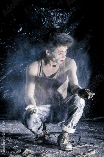 cool dirty vietnamese  guy dancer in style of bboying doing complex tricks on floor in Studio filled with flour on black background. concept of space dance on surface of planet moon photo