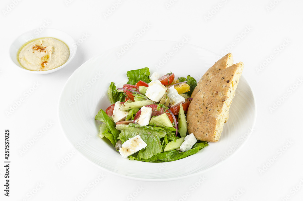 Greek salad with feta cheese, Ligurian olives and tortilla pea and hummus on a plate on a white background Greek salad with feta cheese, Ligurian olives and tortilla pea and hummus on a plate on a white background