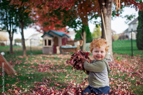 Happy toddler boy playing in backyard about to throw leaves