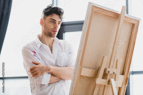 good-looking thoughtful artist in white shirt looking at canvas