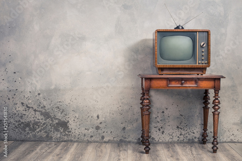 Retro old outdated TV receiver from circa 50s on wooden table front textured concrete wall background. Vintage style filtered photo photo