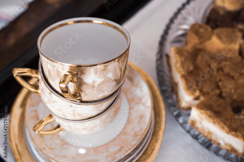 Beautiful golden empty teacups and cake, waiting for dessert to be served