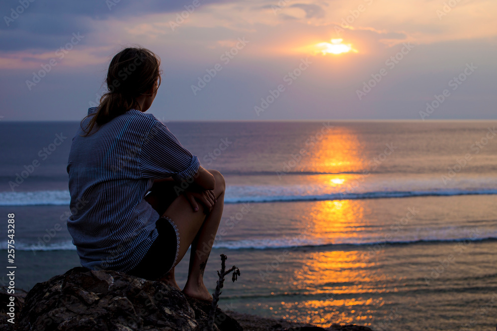 Woman sitting on rock at the beach and looking sunset view Stock Photo ...
