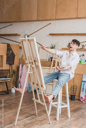 excited artist sitting on high chair at easel with canvas