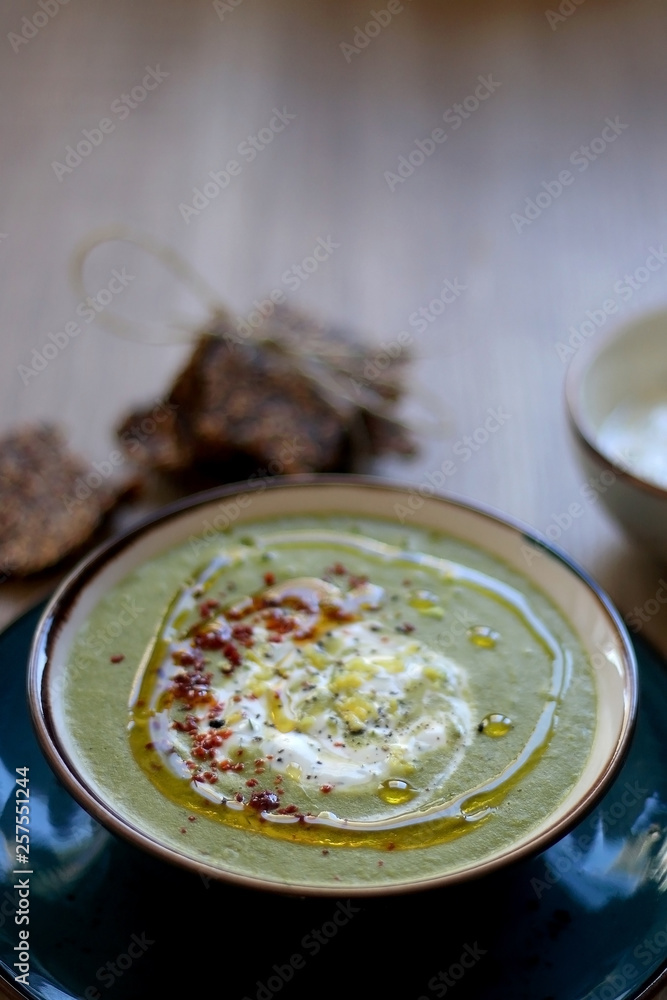 Creamy vegetable soup with kale, cabbage, celery and millet, decorated with olive oil, yoghurt sauce and chilli flakes. Served with seed crackers and lemony yoghurt sauce. Selective focus. Creamy vegetable soup with kale, cabbage, celery and millet, decorated with olive oil, yoghurt sauce and chilli flakes. Served with seed crackers and lemony yoghurt sauce. Selective focus.