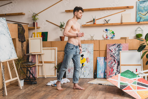 handsome half-naked artist in blue jeans standing in spacious light painting studio