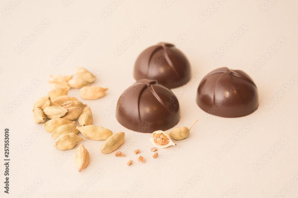 Three artisan dark chocolate sweets isolated on white background, with the ingredient of the filling at view: aromatic cardamom pods and seeds Three artisan dark chocolate sweets isolated on white background, with the ingredient of the filling at view: aromatic cardamom pods and seeds