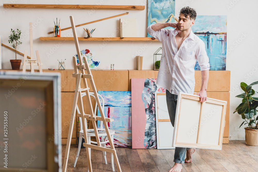 selective focus of handsome barefoot artist carrying canvas in painting studio selective focus of handsome barefoot artist carrying canvas in painting studio
