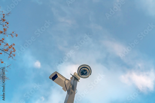Security cameras against cloudy blue sky and tree