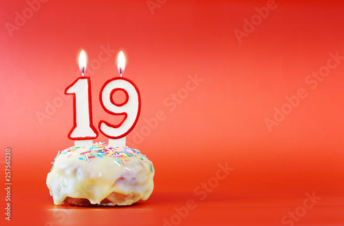 Nineteen years birthday. Cupcake with white burning candle in the form of number 19. Vivid red background with copy space