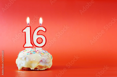 Sixteen years birthday. Cupcake with white burning candle in the form of number 16. Vivid red background with copy space
