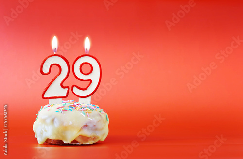 Twenty nine years birthday. Cupcake with white burning candle in the form of number 29. Vivid red background with copy space