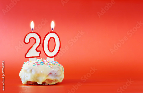 Twenty years birthday. Cupcake with white burning candle in the form of number 20. Vivid red background with copy space
