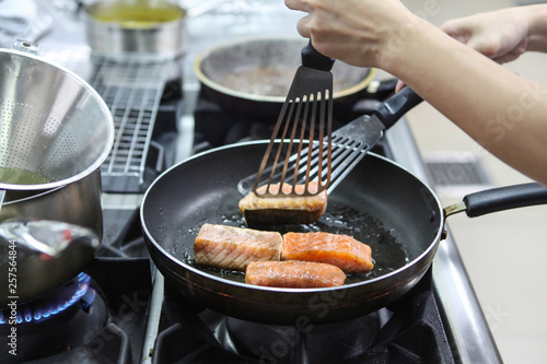 The chef is frying salmon in the pan in the kitchen.
