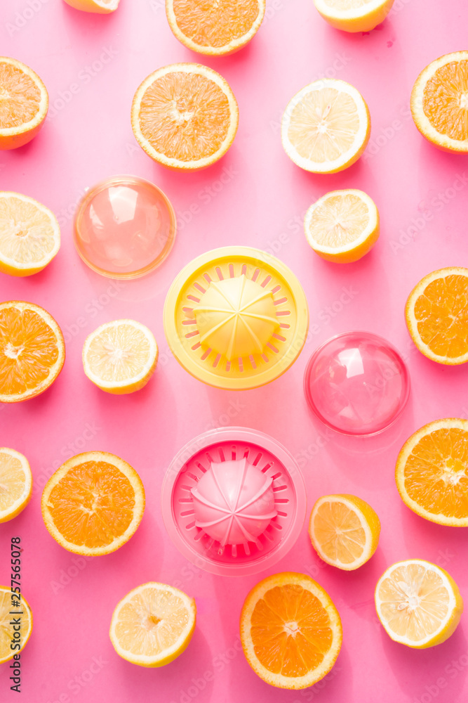 Orange and lemon juice maker, fresh summer juice, cut lemon and orange fruit with red and yellow juice container and squeezer,top view, on a pink board with strong backlight Orange and lemon juice maker, fresh summer juice, cut lemon and orange fruit with red and yellow juice container and squeezer,top view, on a pink board with strong backlight