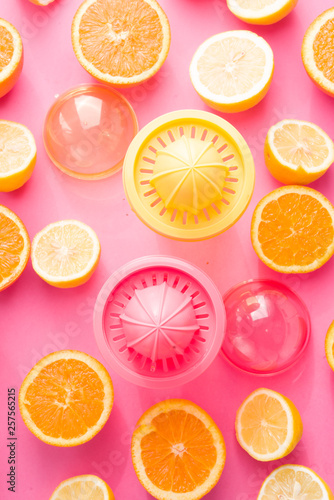 Orange and lemon juice maker  fresh summer juice  cut lemon and orange fruit with red and yellow juice container and squeezer top view  on a pink board with strong backlight