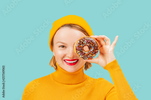 Happy woman with colorful donut against her eyes on pastel blue background photo