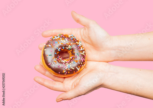 Female hands holding colorful donut on pastel pink background