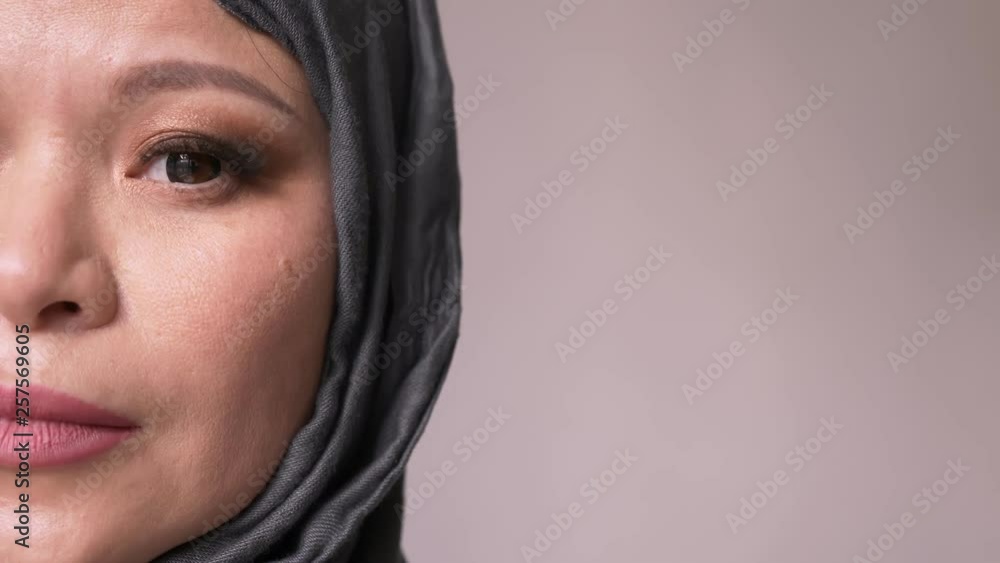 Closeup half-face shoot of adult attractive muslim female in hijab looking forward and turning to camera with isolated background Closeup half-face shoot of adult attractive muslim female in hijab looking forward and turning to camera with isolated background