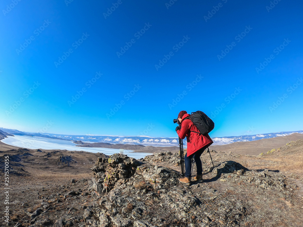 Fototapeta premium camera man in bright orange winter jacket takes landscape photo of Baikal lake in Russia