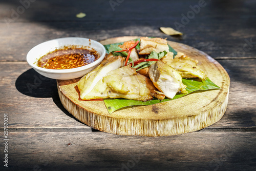 Grilled chicken with chili sauce on banana leaf and wooden background.Thai traditional menu.