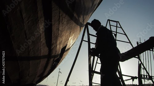 Worker repairing a fishing boat in the fishing port of Essaouira, on Morocco's Atlantic coast. photo