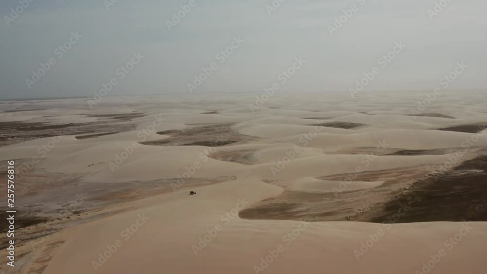 Aerial: A truck with kitesurfers traveling through the dunes of Lencois Maranhenses in Brazil, during dry season. Aerial: A truck with kitesurfers traveling through the dunes of Lencois Maranhenses in Brazil, during dry season.