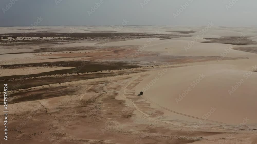 Aerial: A truck with kitesurfers traveling through the dunes of Lencois Maranhenses in Brazil, during dry season. Aerial: A truck with kitesurfers traveling through the dunes of Lencois Maranhenses in Brazil, during dry season.