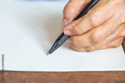 Senior woman's left Hand writing letter on ivory paper background, Notebook, A black pen, Close up & Macro shot, Selective focus, Stationery concept