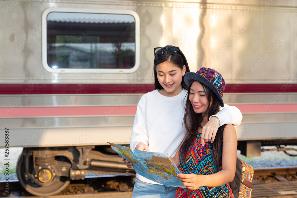 Two women are holding the map while waiting for the train. Tourism concept