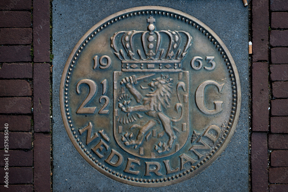 Impression of Dutch two-and-a-half guilder coin embedded as decoration in pavement. Monument to the currency from before the Euro was introduced in 2002. Impression of Dutch two-and-a-half guilder coin embedded as decoration in pavement. Monument to the currency from before the Euro was introduced in 2002.