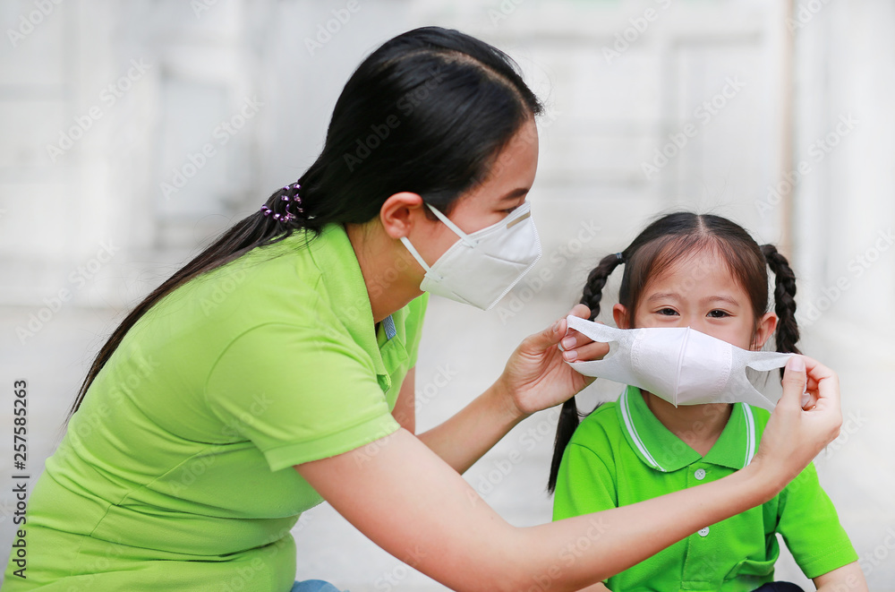 Asian young mother wearing protective mask for her daughter while outside to against PM 2.5 air pollution in Bangkok city. Thailand. Asian young mother wearing protective mask for her daughter while outside to against PM 2.5 air pollution in Bangkok city. Thailand.
