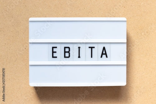 White lightbox with word EBITA (abbreviation of  earnings before interest, taxes and amortization) on wood background photo