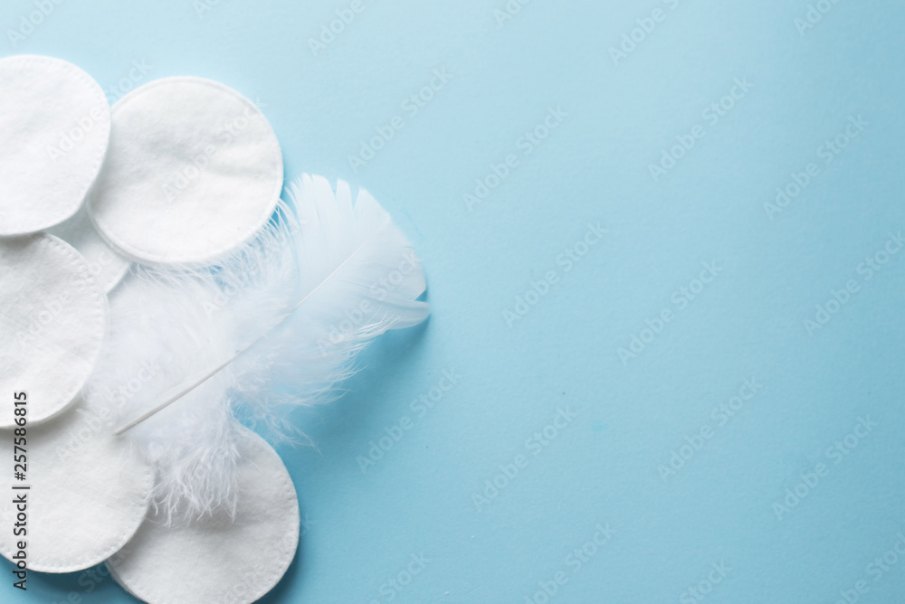 cotton pads with white feather on blue background close up . copy space. top view cotton pads with white feather on blue background close up . copy space. top view