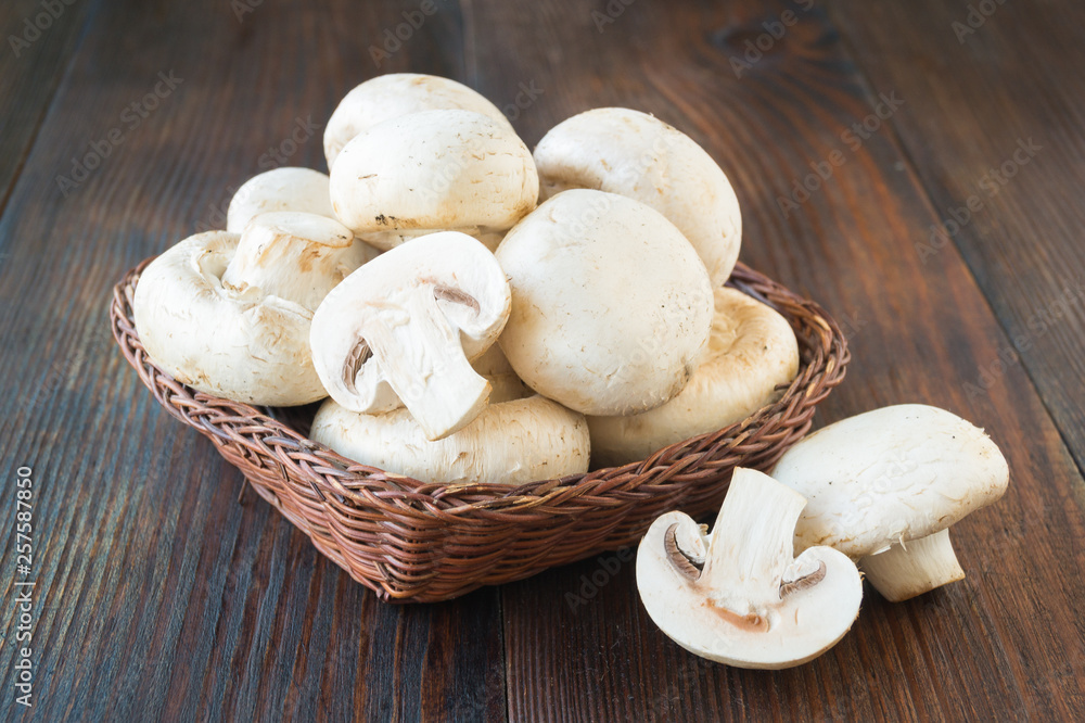 Raw mushrooms in a basket made of twigs on a wooden background Raw mushrooms in a basket made of twigs on a wooden background