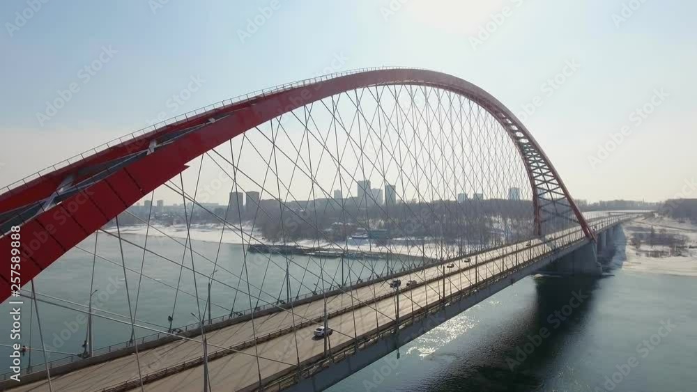 Helicopter shot beside suspension red brigde with medium traffic cars driving across the road. industrial concept, sunny shining day. City landscape with fog and scyscrappers behind. drone shot 4k Helicopter shot beside suspension red brigde with medium traffic cars driving across the road. industrial concept, sunny shining day. City landscape with fog and scyscrappers behind. drone shot 4k