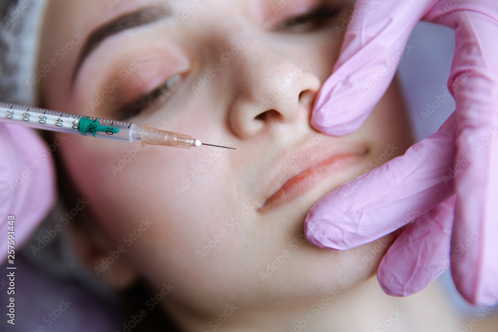 The doctor cosmetologist makes the Rejuvenating facial injections procedure for tightening and smoothing wrinkles on the face skin of a beautiful, young woman in a beauty salon. The doctor cosmetologist makes the Rejuvenating facial injections procedure for tightening and smoothing wrinkles on the face skin of a beautiful, young woman in a beauty salon.