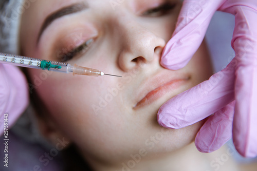 The doctor cosmetologist makes the Rejuvenating facial injections procedure for tightening and smoothing wrinkles on the face skin of a beautiful, young woman in a beauty salon.