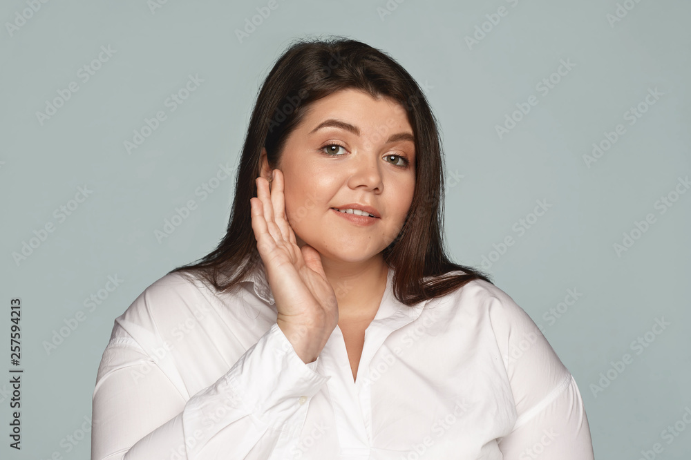 People, lifestyle and beauty concept. Isolated shot of cute charming young brunette overweight female employee in white shirt applying moisturizer on face before work for shiny glowing skin People, lifestyle and beauty concept. Isolated shot of cute charming young brunette overweight female employee in white shirt applying moisturizer on face before work for shiny glowing skin