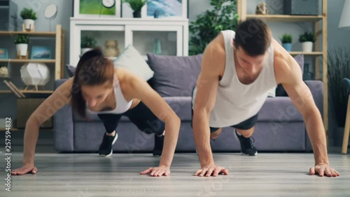 Wallpaper Mural Beautiful couple young girl and guy are exercising together doing pushups and clapping hands at home. People, healthy lifestyle and relationship concept. Torontodigital.ca