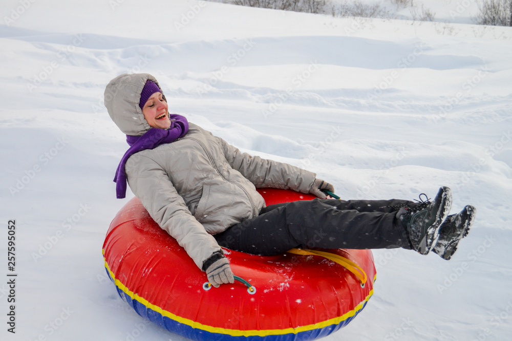 A girl with a smile riding down a hill in an inflatable bagel in winter