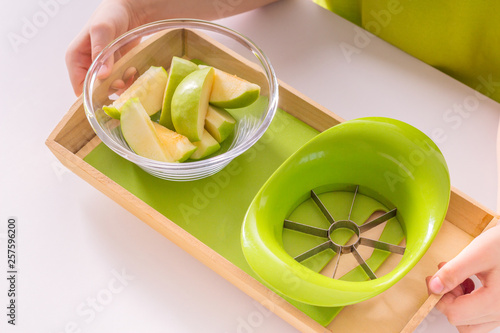 Children's hands hold a wooden tray with montessori materials for a lesson from the practical life zone. Apple slicer, cutting board,green apple. Isolate on white background. photo