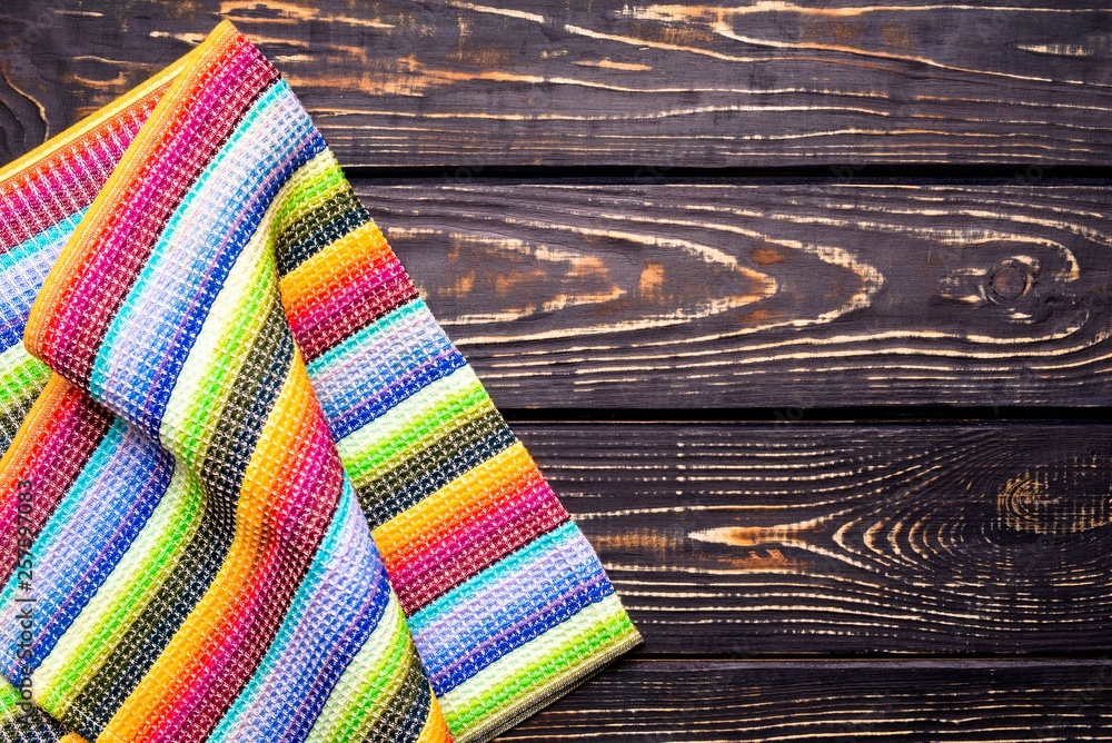 The colorful tablecloth is a brown wooden table The colorful tablecloth is a brown wooden table