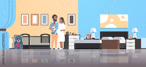 husband with pregnancy wife holding newborn baby son standing near crib happy african american family parenthood concept modern home bedroom interior flat full length