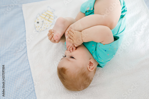 Cute baby taking feet in mouth. Adorable little baby girl sucking own foot. Healthy child on changing table. Happy daughter.