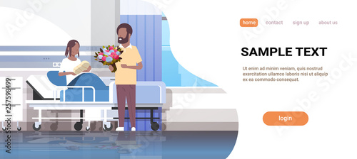 husband holding flowers bouquet for his wife with newborn baby loving father visiting new born child african american family parenthood concept hospital ward interior horizontal copy space