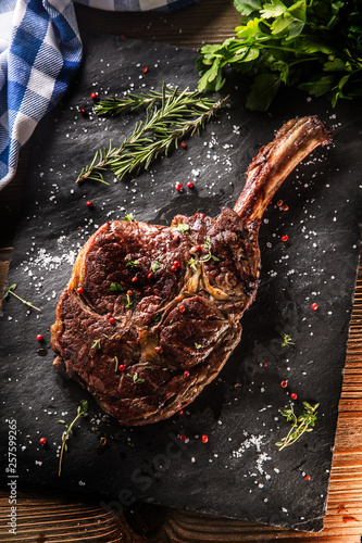 Fotografie Freshly grilled tomahawk steak on slate plate with salt pepper rosemary and pars