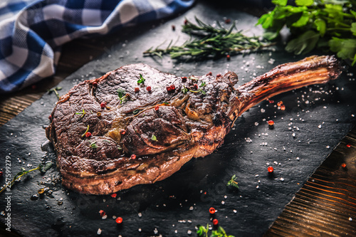 Freshly grilled tomahawk steak on slate plate with salt pepper rosemary and parsley herbs photo