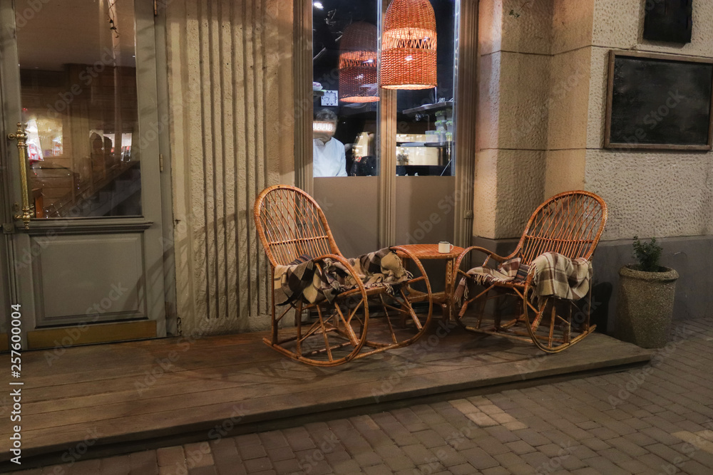 Naklejka premium Rustic Sidewalk Cafe with Wooden Tables, Flower Pot and Plaids on Wicker Chair Outdoors